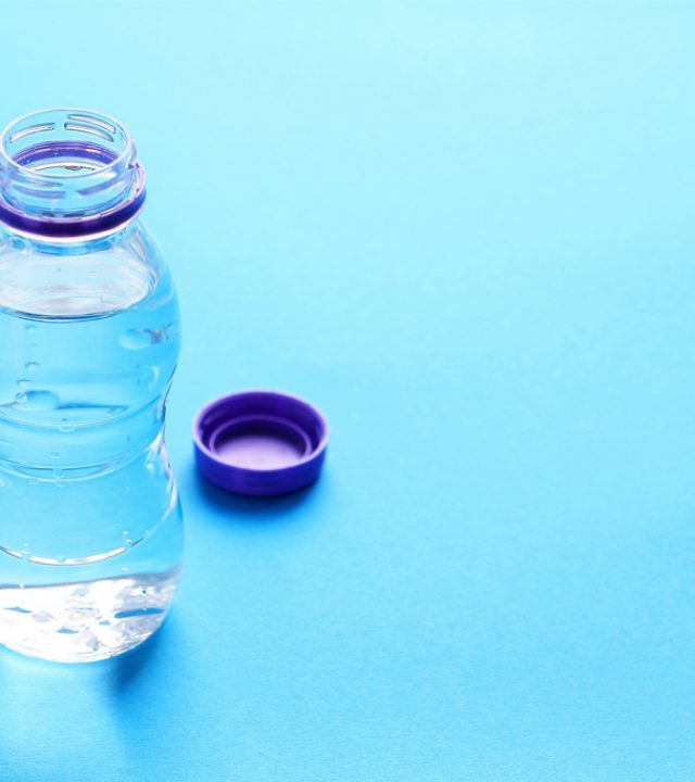 Open plastic bottle with water on a blue background. The concept of environmental protection. Close-up, copy space.
